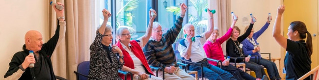 Aged persons doing arm exercises while seated in care facility