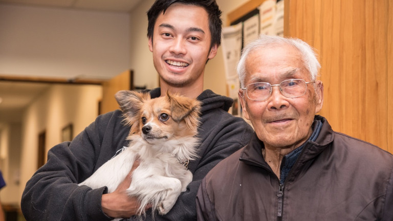 Elderly man with visitor holding dog in retirement village corridor