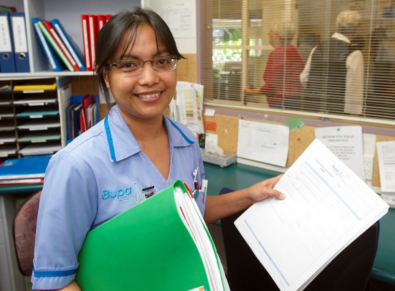 Migrant aged care worker in office holding a file and smiling