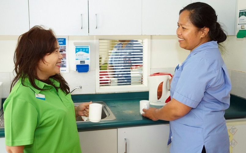 Two migrant aged care workers chatting in the kitchen during a break