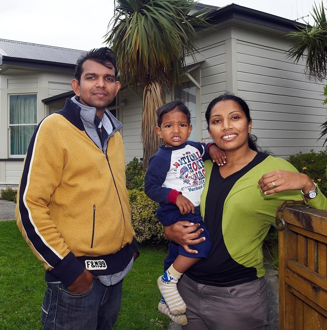 Migrant parents standing in front of house holding toddler