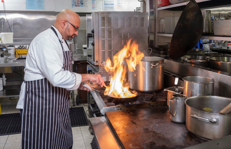Chef cooking in kitchen with flambe above pan