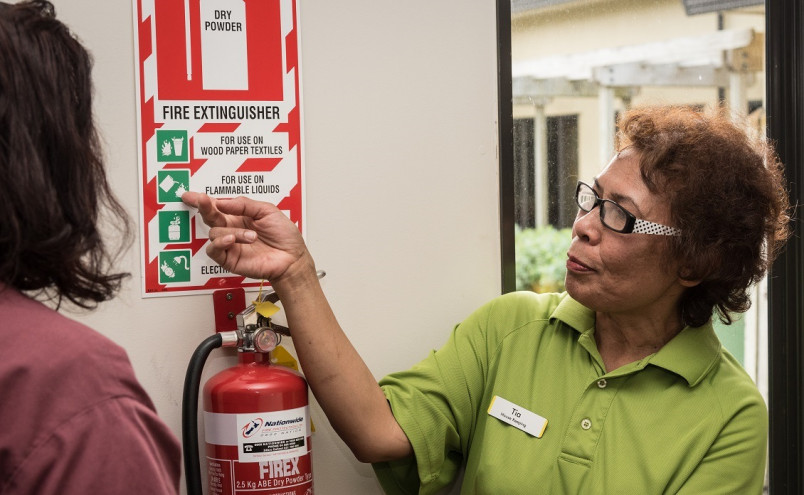 Aged care worker explaining fire extinguisher instructions to a new migrant worker 