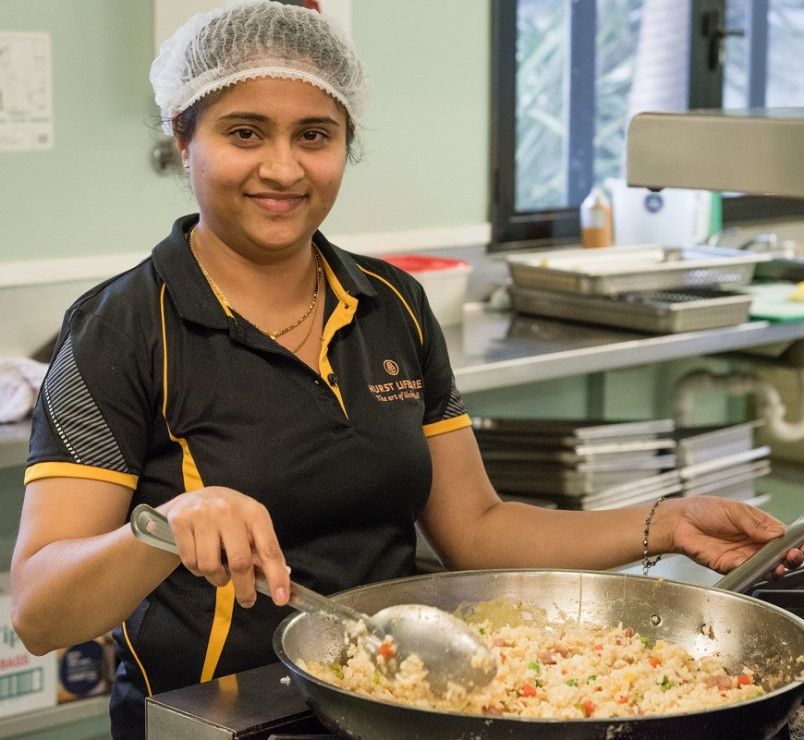 Aged care village cook holding a wok filled with fried rice.